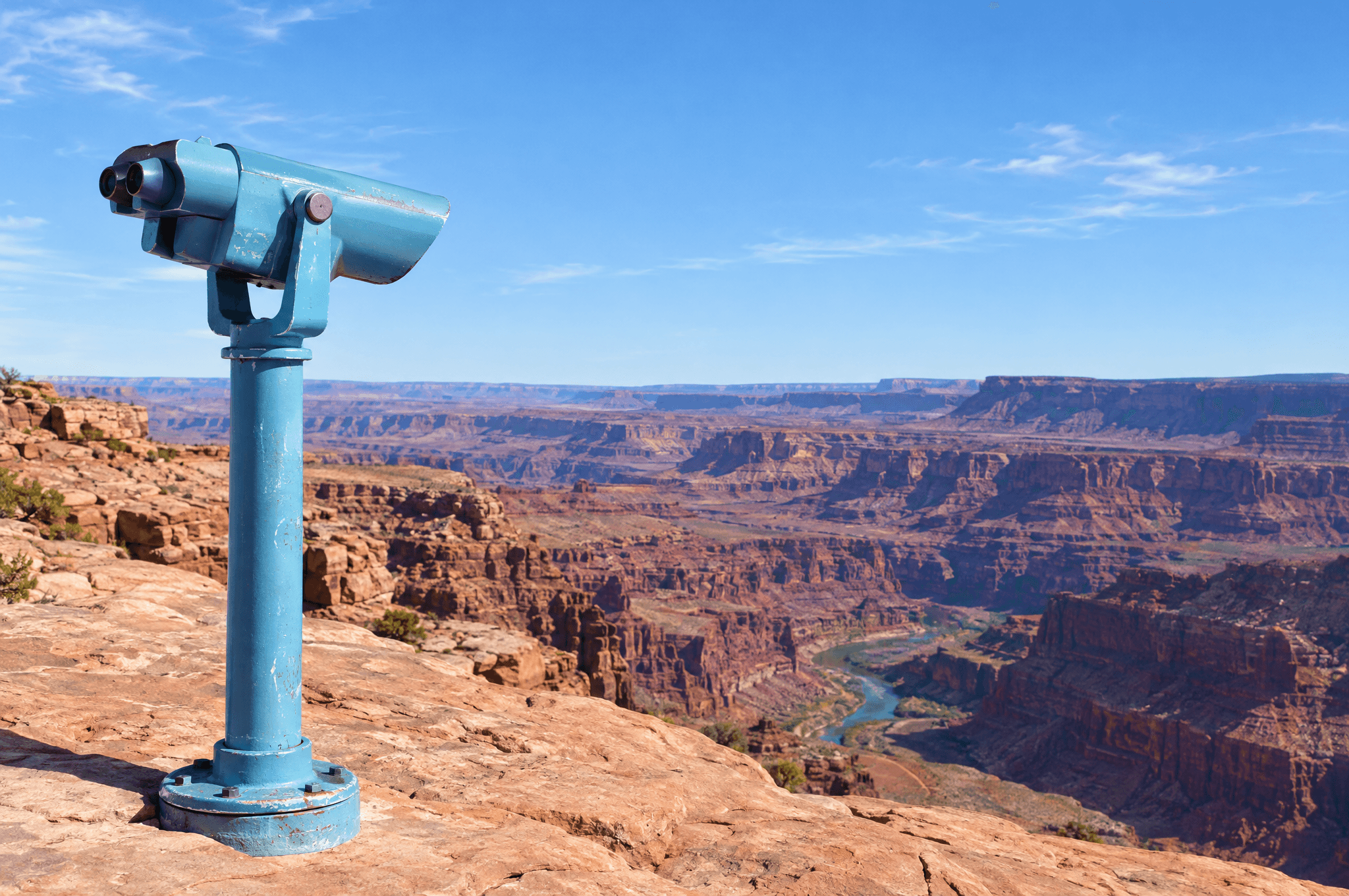 A coin-operated viewer on a post at a sandstone overlook, pointed out across a red rock canyon under a clear blue sky.
